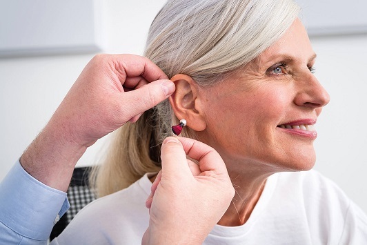 Ältere Frau erhält ein modernes Hörgerät, Hörakustiker passt Hörhilfe im Ohr an.